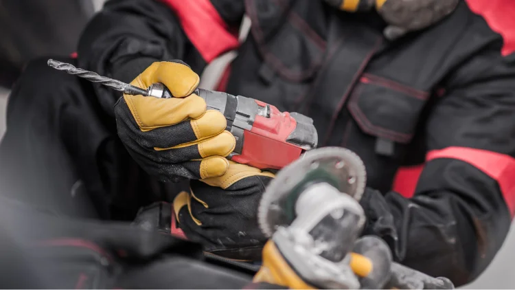 Worker using an electric drill with safety gloves on a construction site